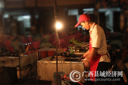 入夜,平果街头的烧烤摊点成了市民的休闲好去处,图中的烧烤师傅正在精心调制美食.jpg